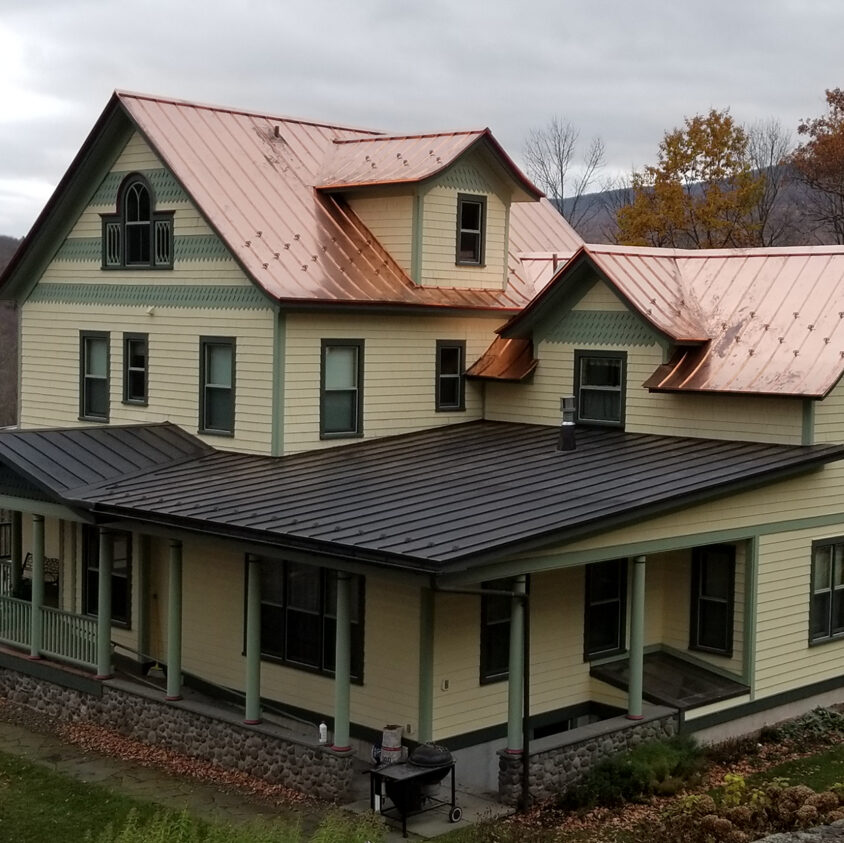 light yellow house with copper and mixed metal roof