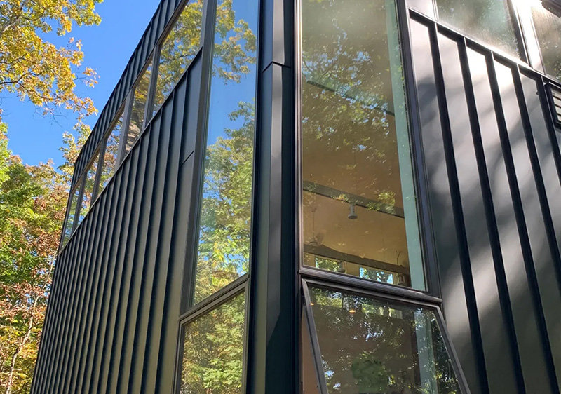 Close up of square modern home featuring a standing seam metal roof and matching metal siding