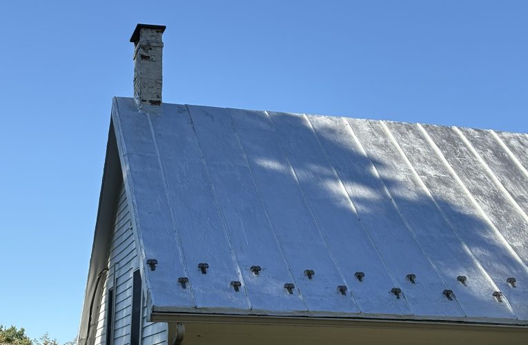 Silver metal roof viewed from the side with a clear blue sky in the background.