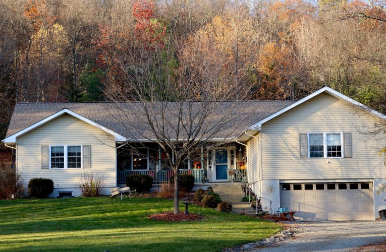 Exterior of a home in Woodstock, NY with a shingle roof, and a forest in the background with autumn leaves.